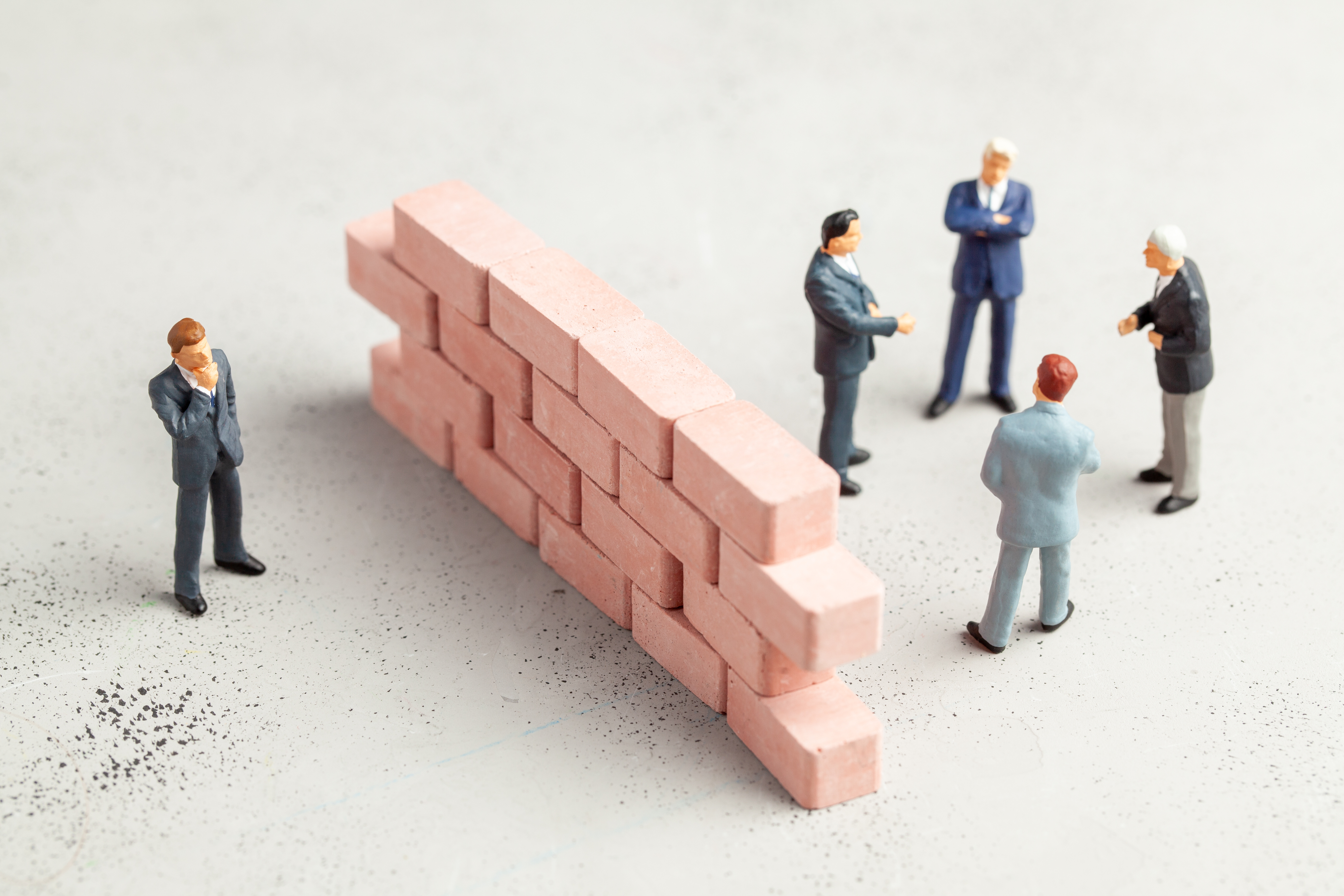 Clay image. One person standing on one side of a brick wall while a group of four people stand on the other side, seemingly talking to each other.
